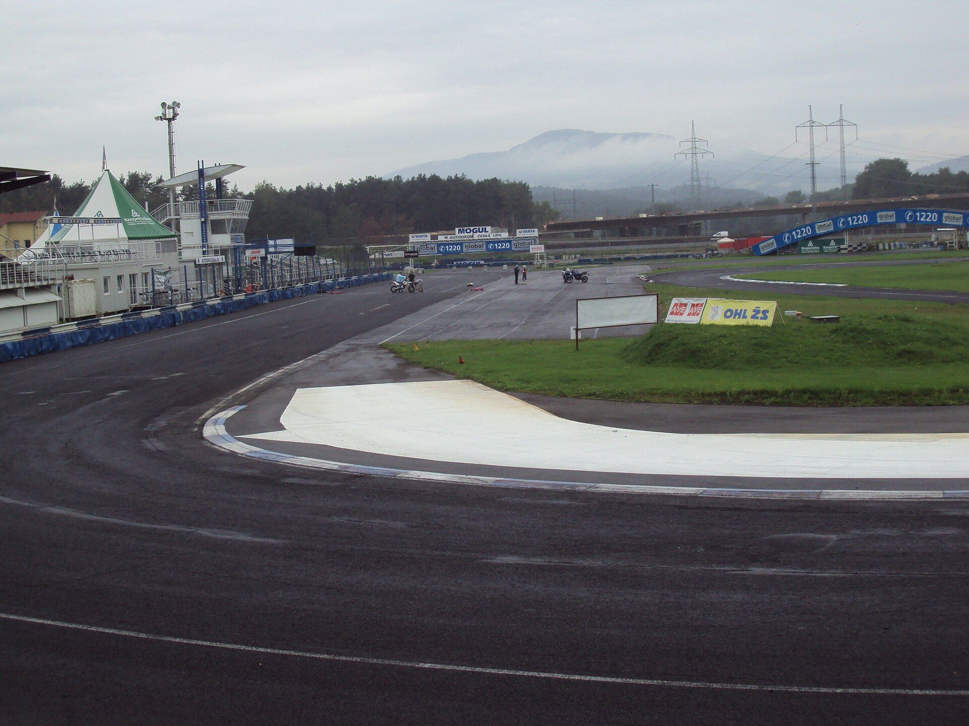 A bend of the Autodrom Sosnová track with a white run-off area, the tower, pavilions and a misty hill behind