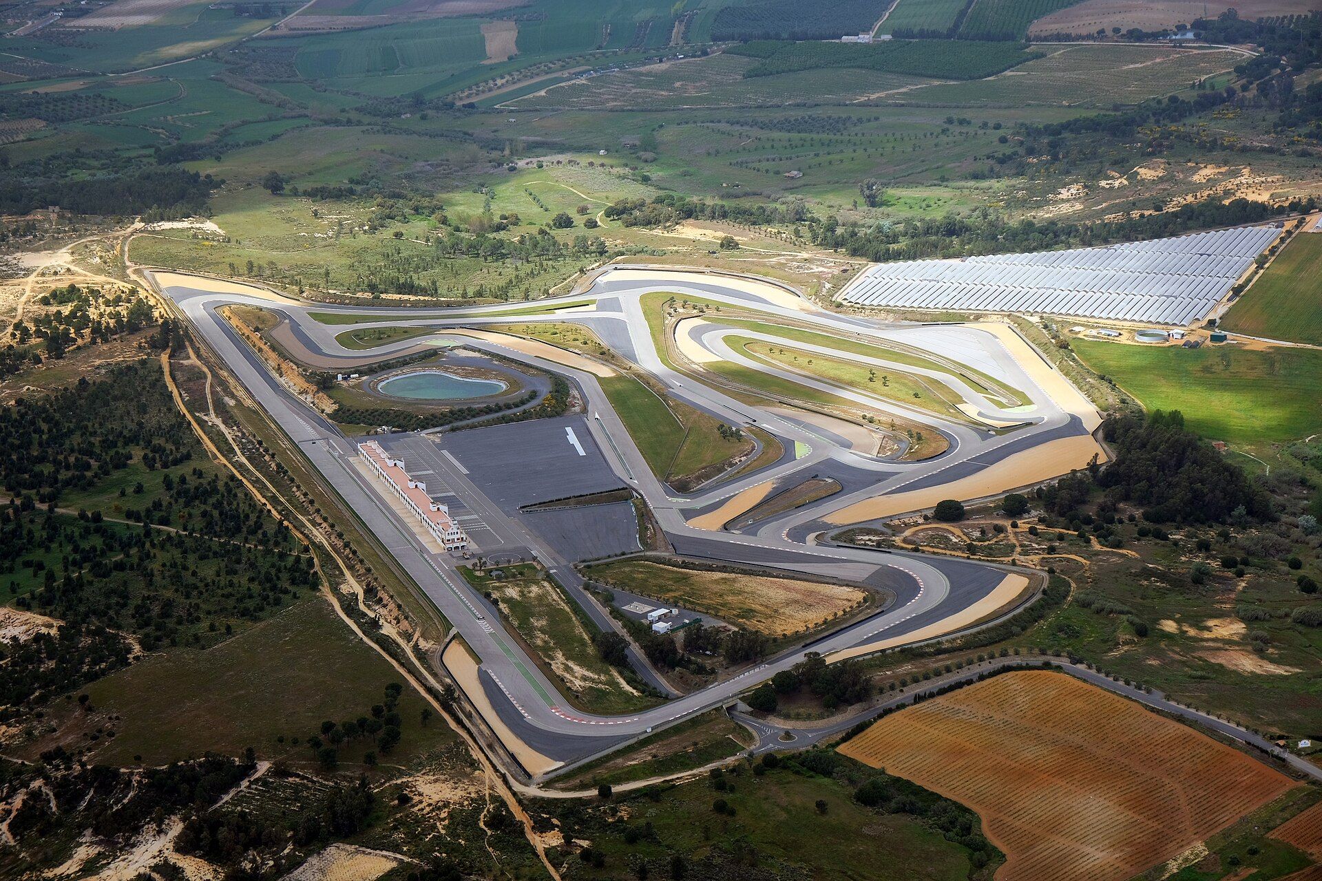 Circuito Monteblanco from the air: the track loop with the pit building and a car park in the middle, surrounded by fields, groves and a solar farm