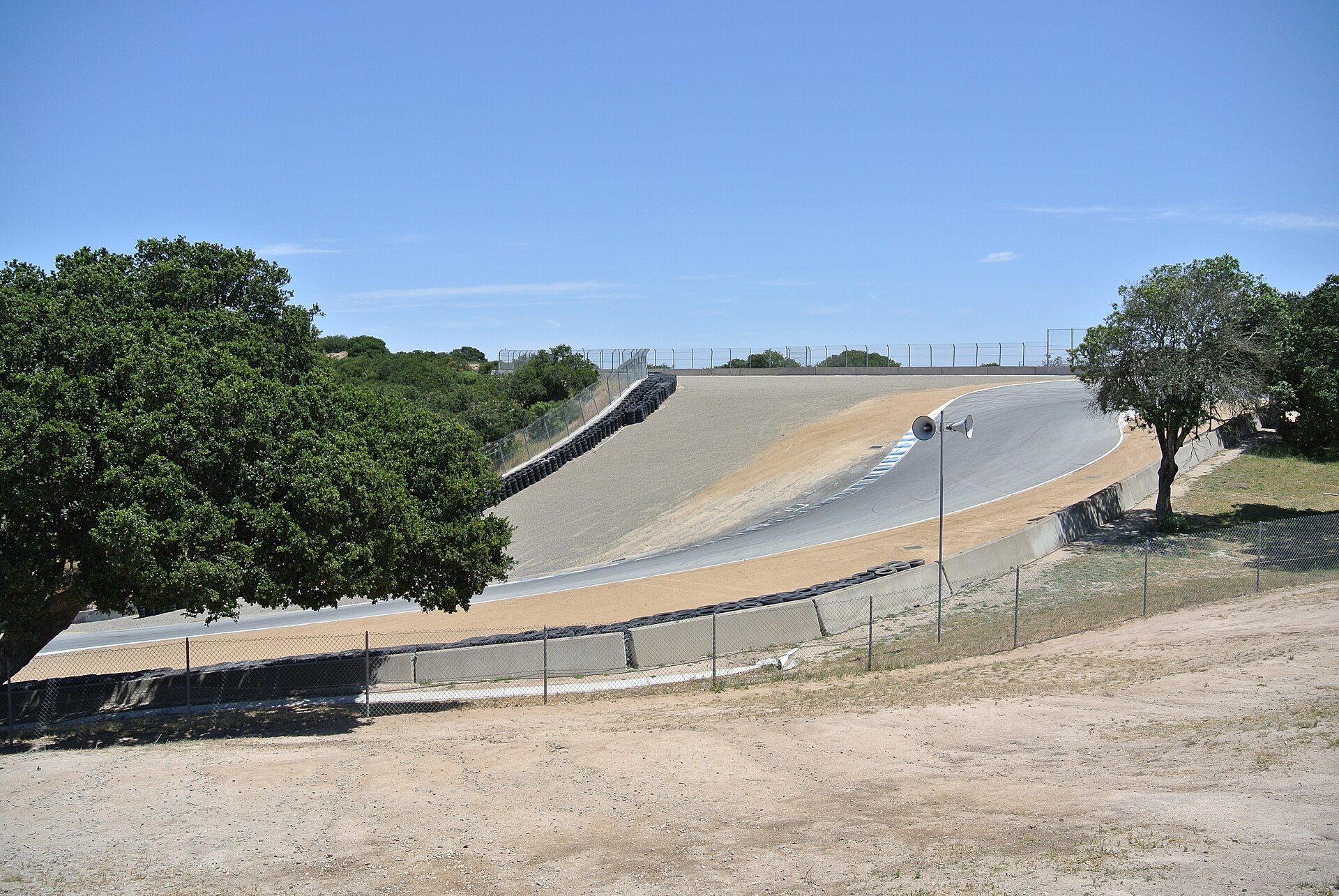 The Corkscrew at Laguna Seca seen from below: the asphalt drops steeply between concrete barriers and a tyre wall, with trees and dry grass around