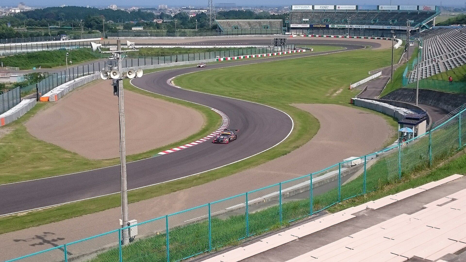 The S-curves at Suzuka seen from a grandstand: a racing car in the corner, with more of the track and grandstands behind