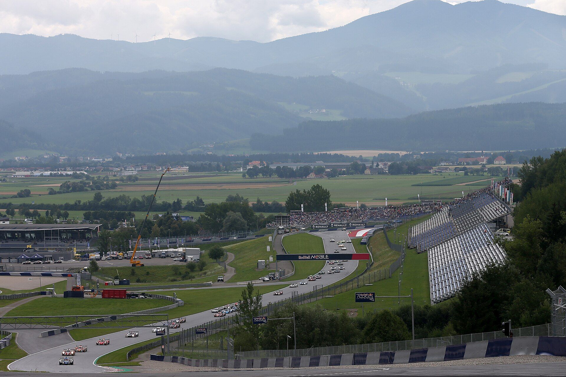 Der Red Bull Ring von einem erhöhten Standpunkt aus während des Rennens der European Le Mans Series 2018: Autos auf der Strecke, rechts eine Tribüne, dahinter das Tal und die Berge